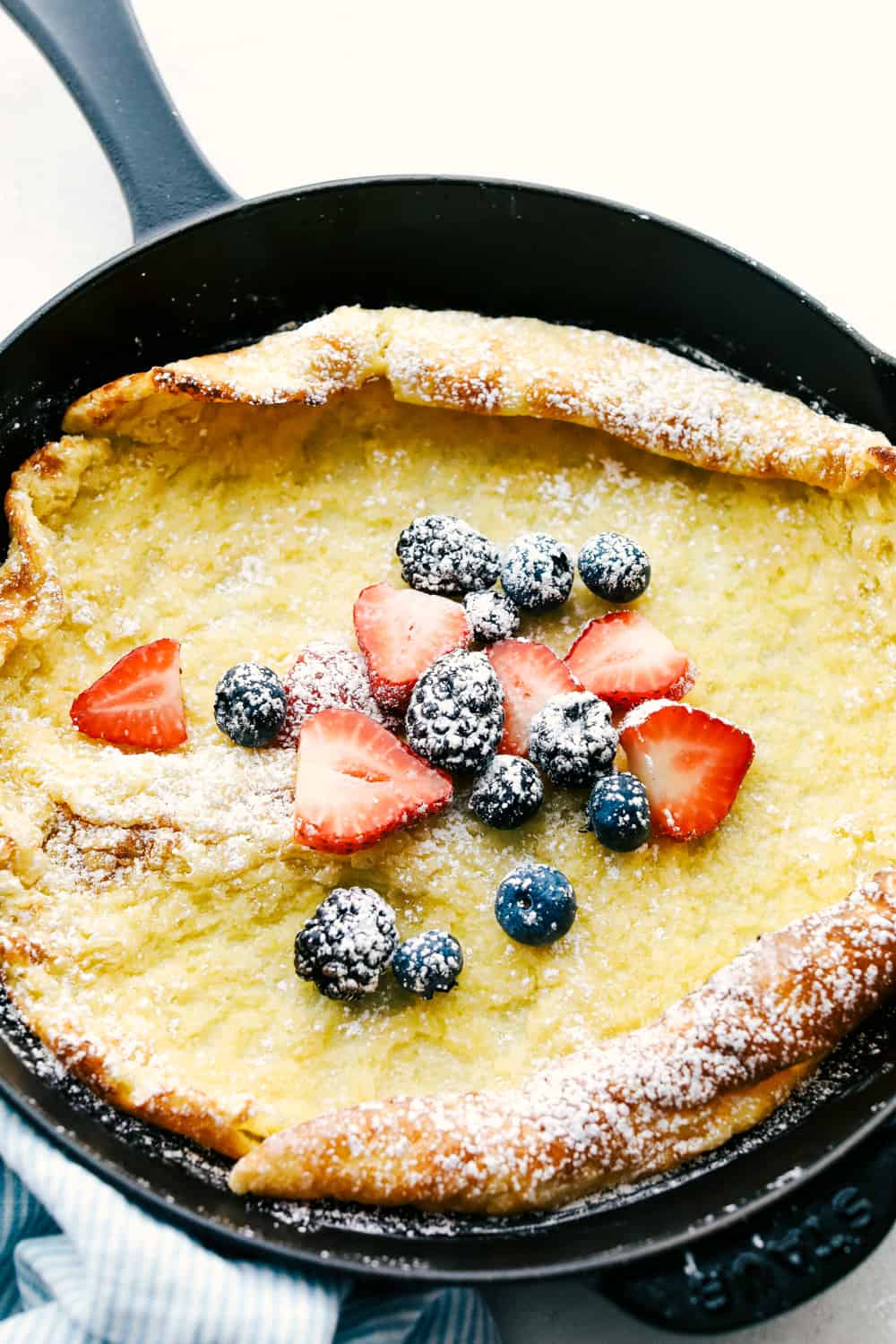 German Oven Pancake is a hot and puffy golden pancake that only requires 5 minutes of prep! This classic breakfast is always a huge hit at our house! German pancake in a frying pan with a variety of berries overtop.